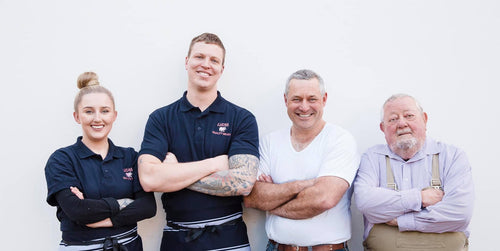 Group portrait of Lucas Meats butchers standing together and smiling against a white wall.