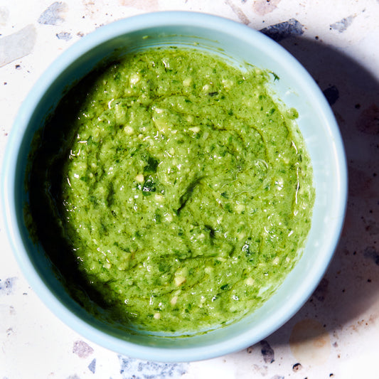 Bowl of vibrant green creamy pesto sauce, freshly made with herbs and natural ingredients.