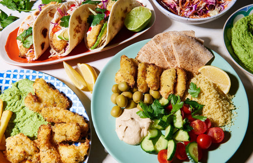 Plates of herby crumbed fish fillets served with tacos, dips, pita, and fresh salad.