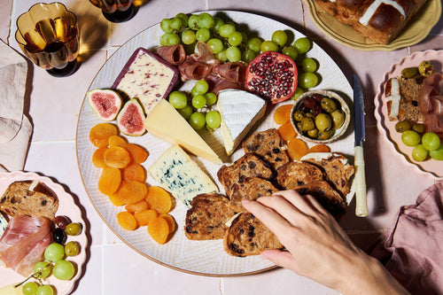 Cheeseboard with hot cross bun crackers, cheese, grapes, figs, and dried fruit.