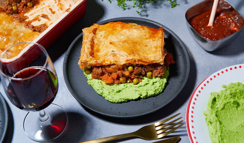Slice of golden pie served on mushy peas with wine and sauce on the side.