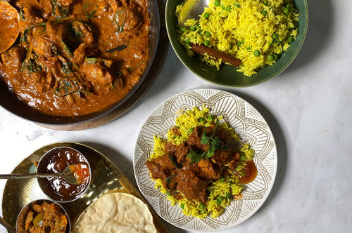Plates of Indian butter chicken served with yellow spiced rice, papadums, and chutneys on the side.