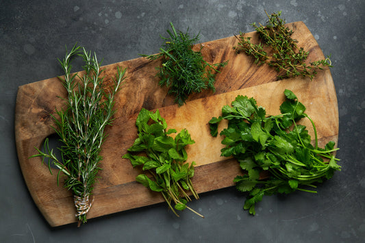 Wooden board with fresh herbs including rosemary, mint, thyme, parsley, and dill.
