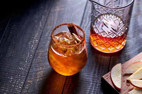 Glass of spiced apple and dark rum cooler with cinnamon stick and sugared rim.