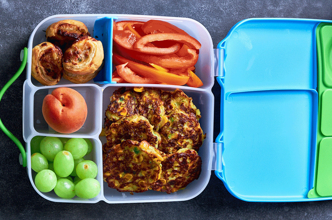 Colourful kids’ lunchbox with fritters, grapes, apricot, capsicum slices, and pastry scrolls – balanced back-to-school meal idea.