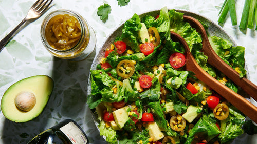Bowl of guacamole salad with avocado, lettuce, cherry tomatoes, corn, and jalapeños.