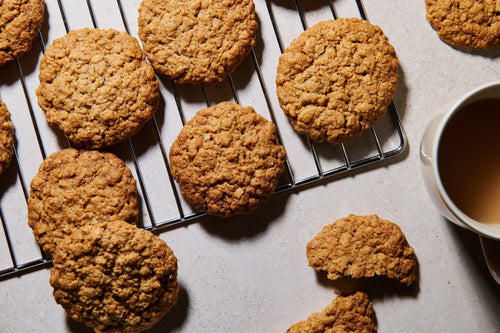 Golden ANZAC biscuits cooling on a rack with a cup of tea nearby.