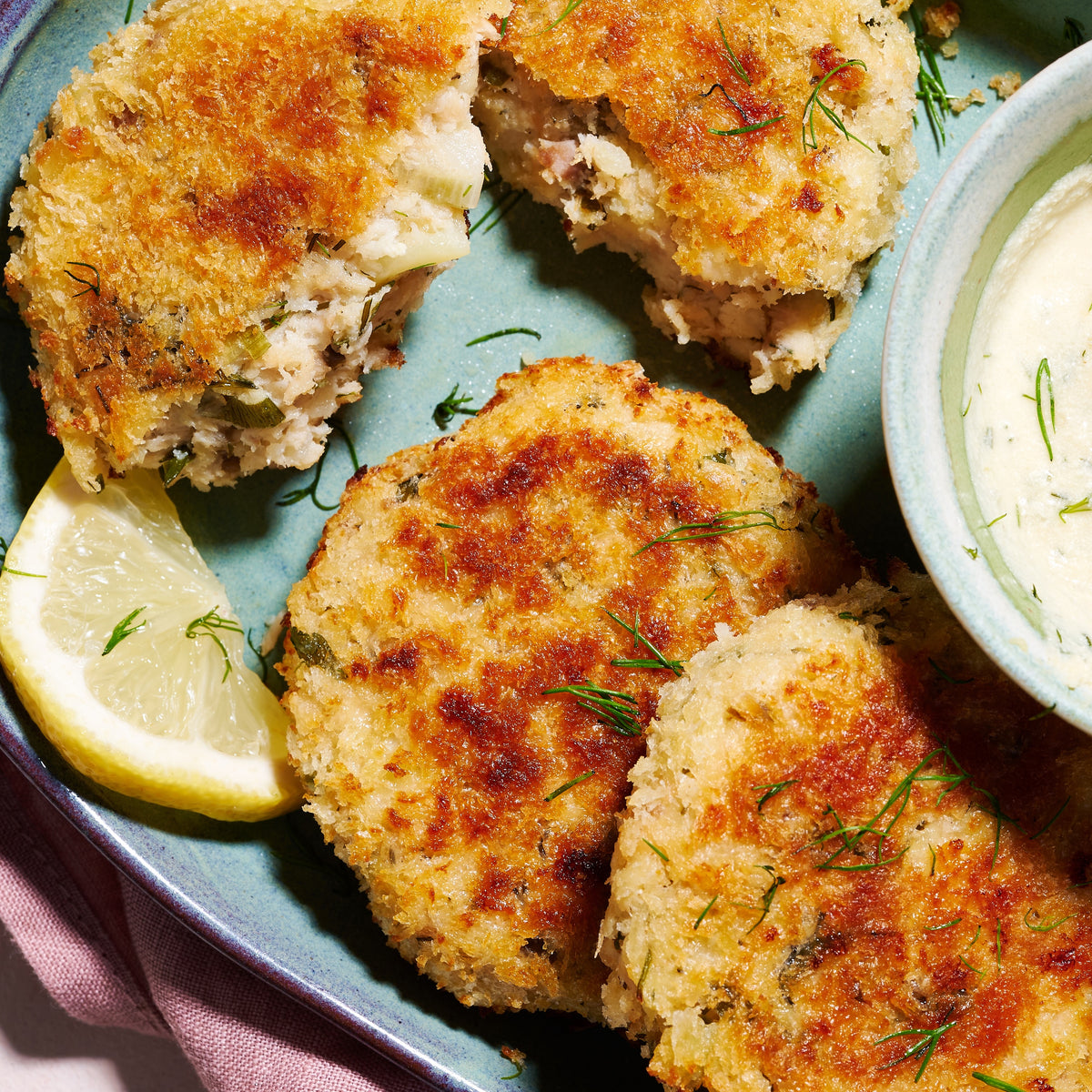 Close-up of Salmon & Barramundi Fish Cakes showing crisp panko crust, herby filling, and lemon wedge garnish.