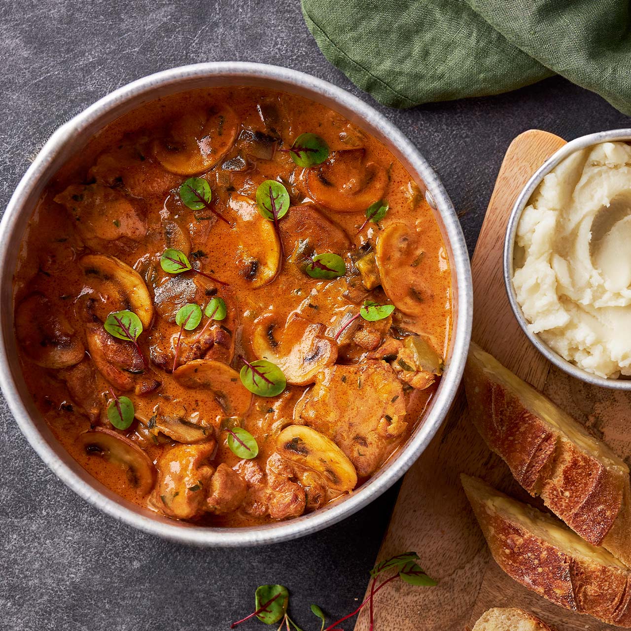 Bowl of creamy Chicken paprikash with mushrooms and paprika, served with mashed potato and crusty bread.