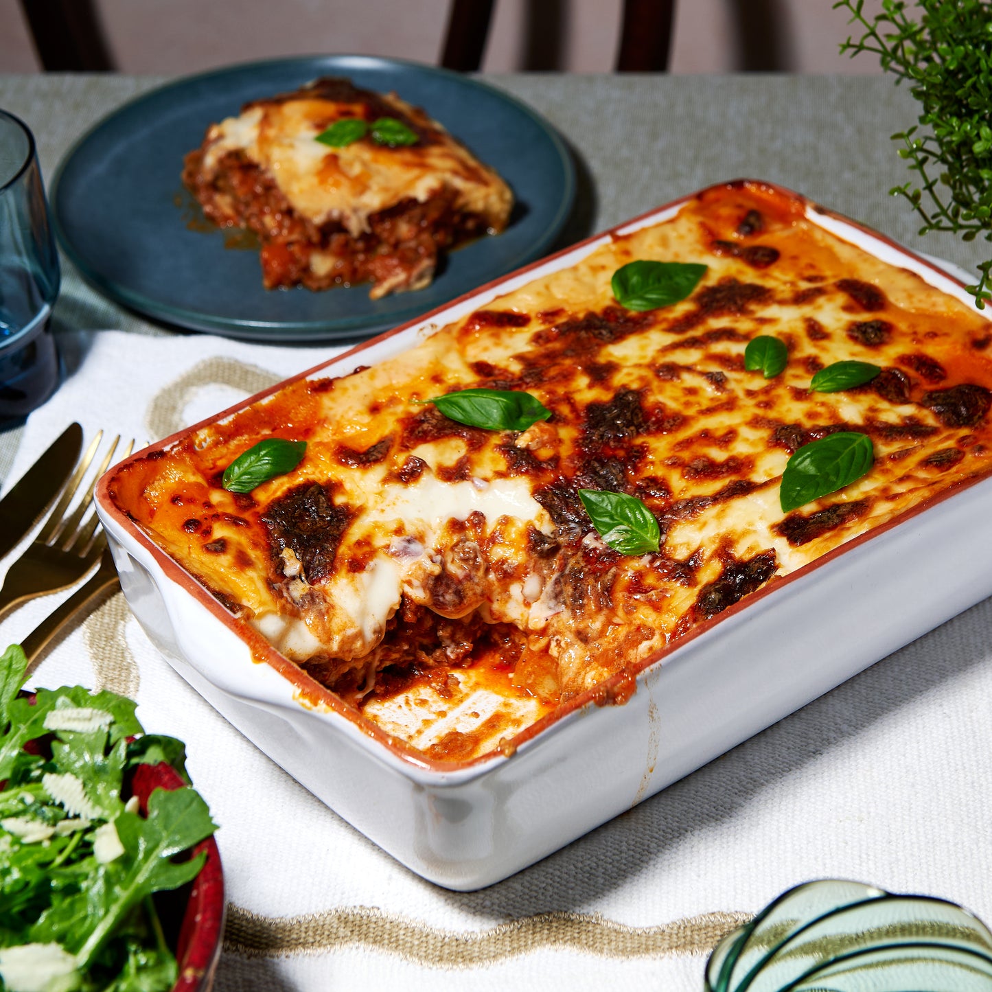 Classic Beef Lasagne in a white baking dish with golden cheese topping and fresh basil.
