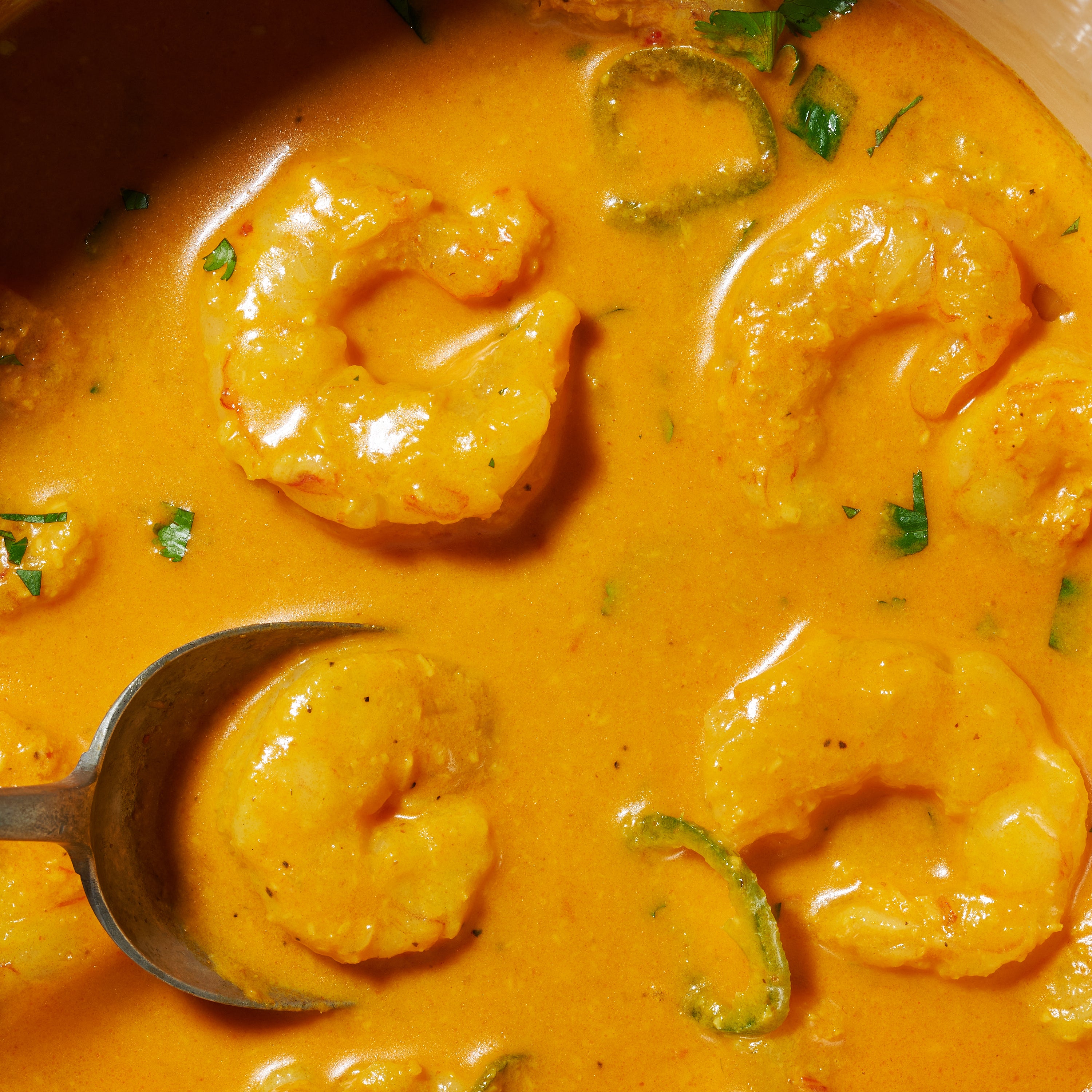 Close-up of prawns simmering in a creamy orange Goan curry sauce with sliced green chilli.
