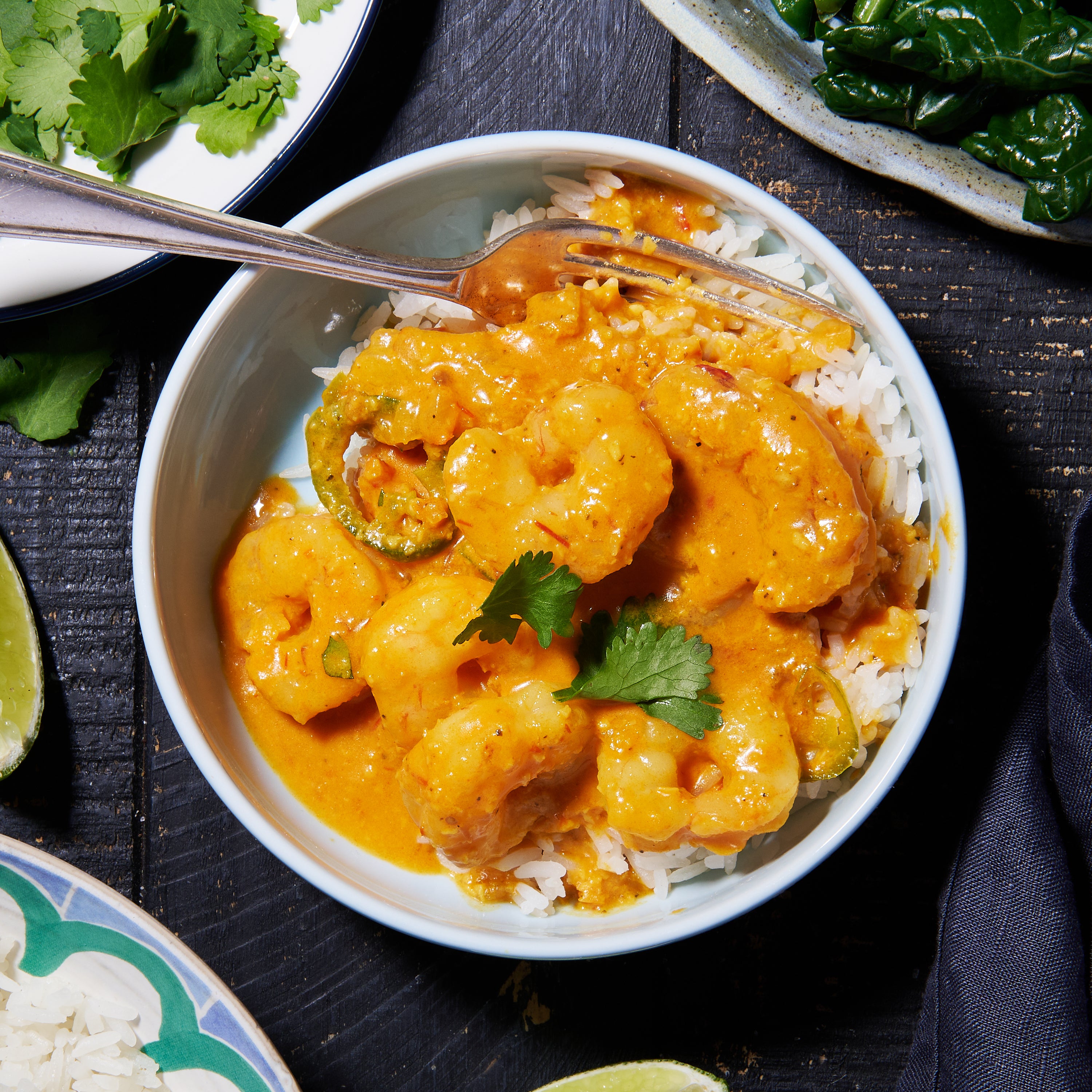 A bowl of Goan prawn curry served over rice, topped with coriander leaves, with lime wedges on the side.