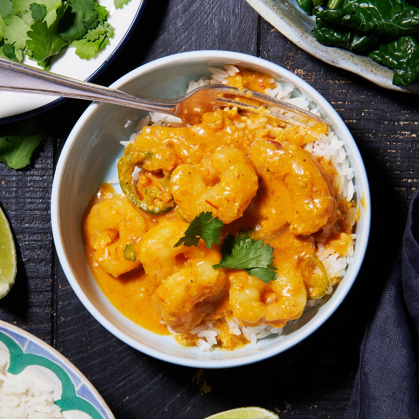 A bowl of Goan prawn curry served over rice, topped with coriander leaves, with lime wedges on the side.