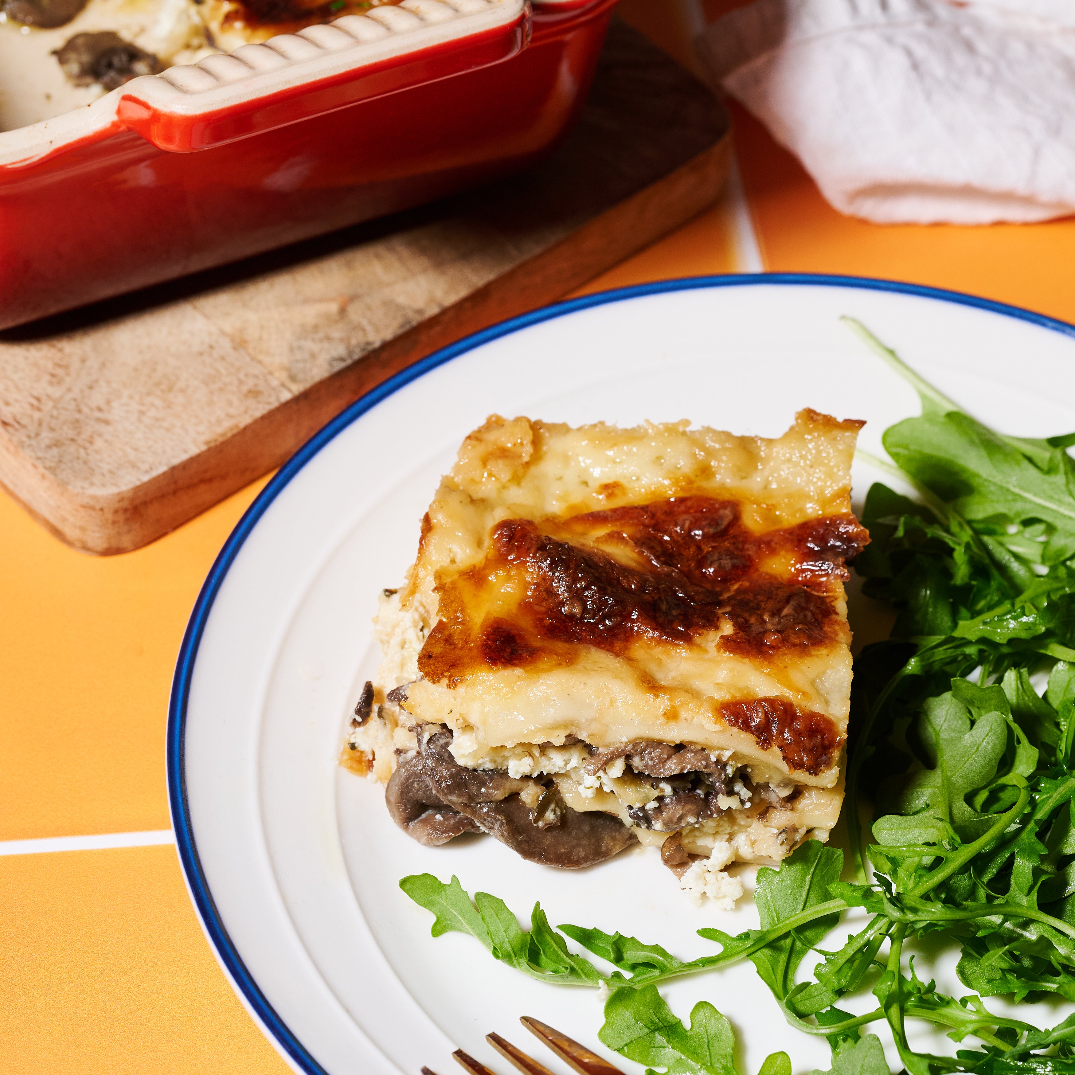 A plated serving of mushroom and ricotta lasagne with truffle salt, paired with fresh rocket salad.