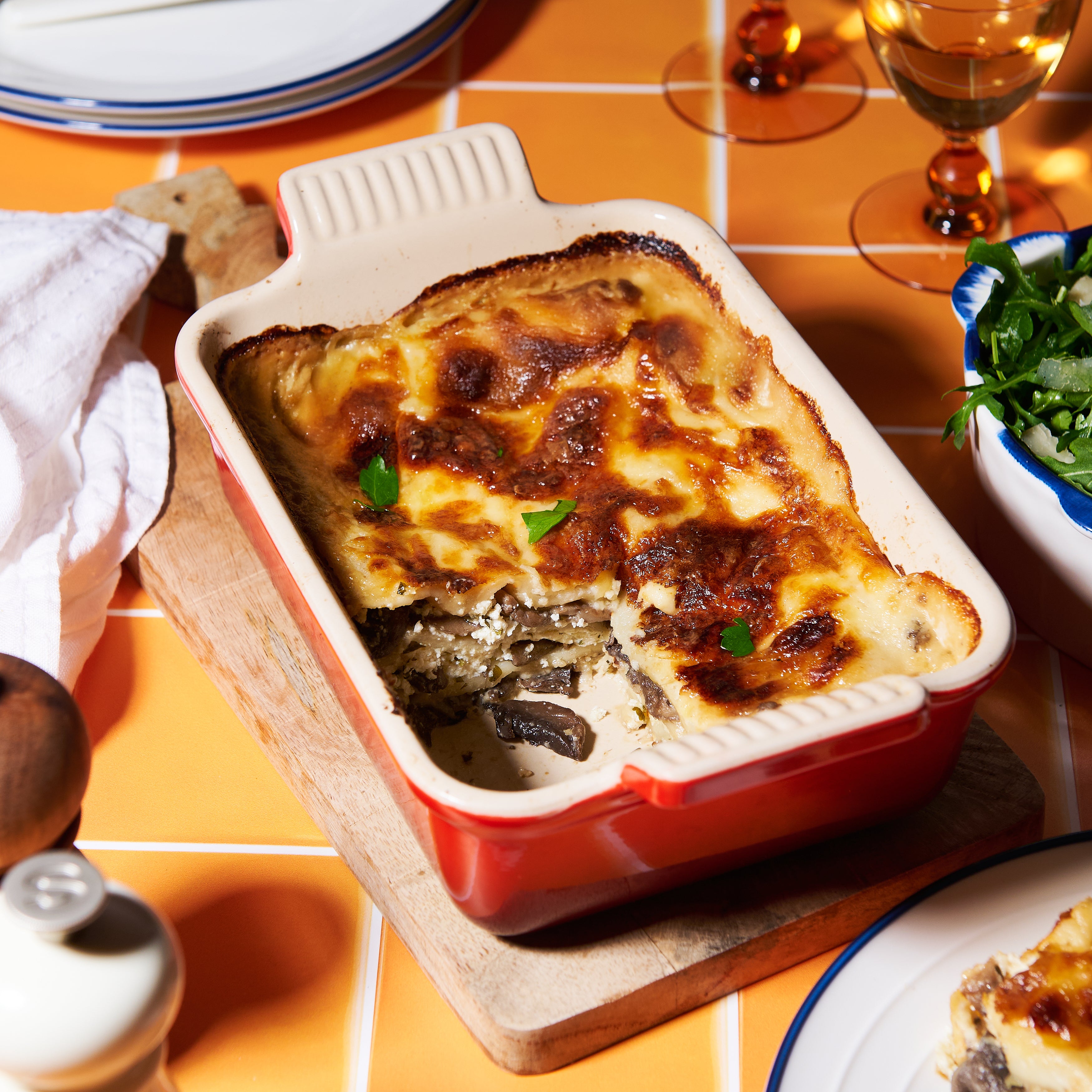 A golden-baked mushroom and ricotta lasagne in a red ceramic dish, with layers of creamy béchamel and melted mozzarella.