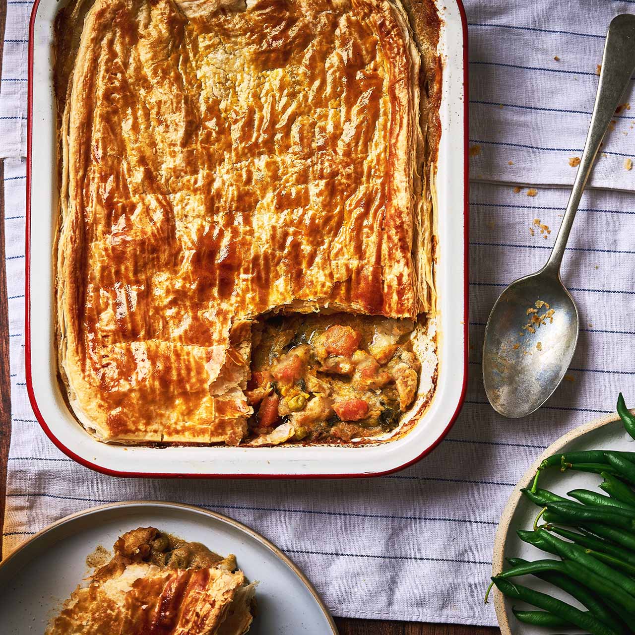 Golden puff pastry-topped Panang vegetable curry pie with a spoonful removed, showing a rich coconut curry filling with mixed vegetables.