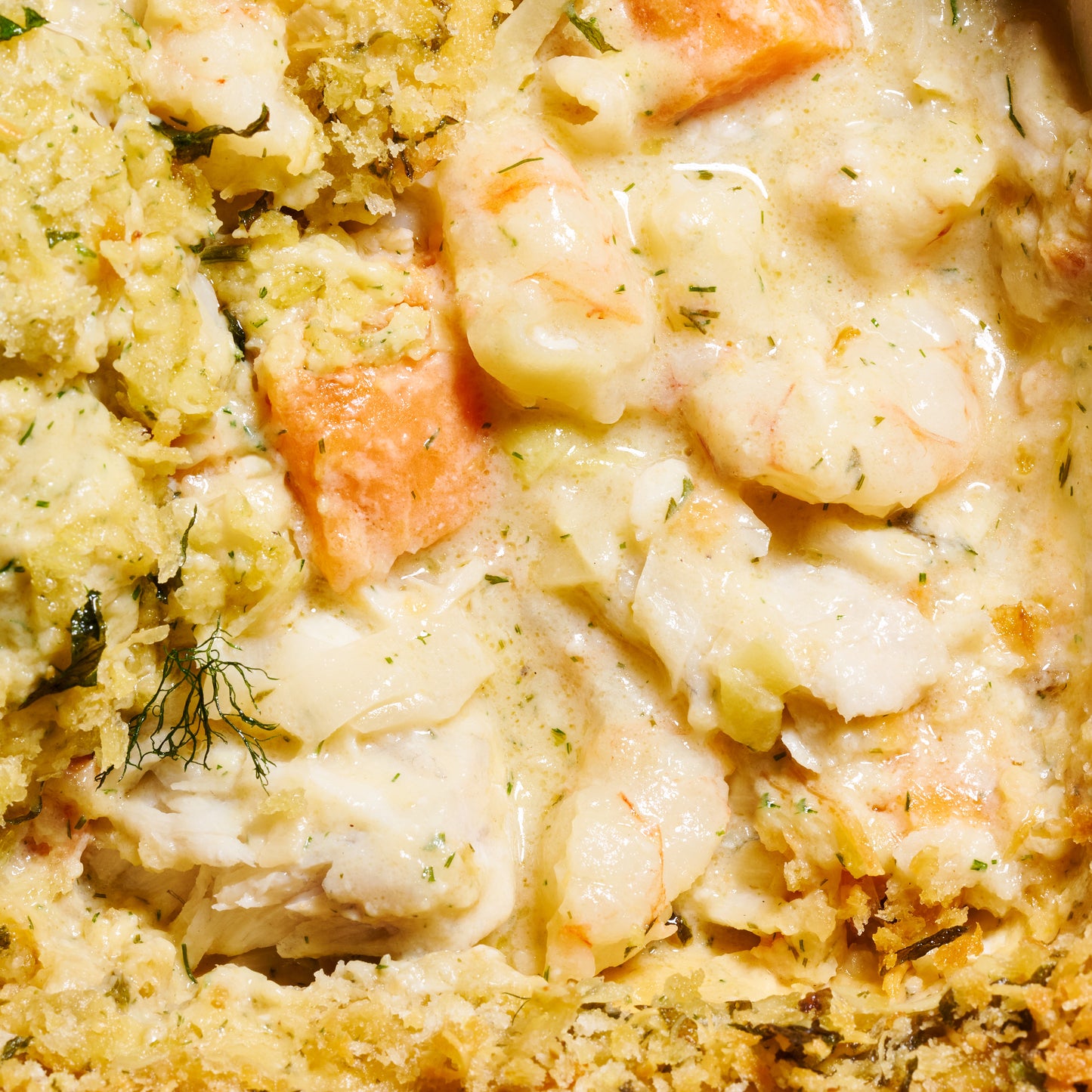 Close-up of Prawn, Leek & Barramundi Gratin showing prawns, barramundi, leeks, and sweet potato in creamy sauce with panko topping.