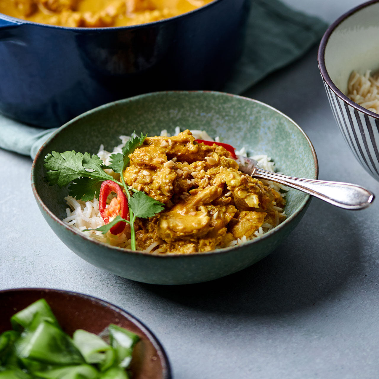 Serving of Satay Chicken curry in a bowl with rice, coriander and red chilli.