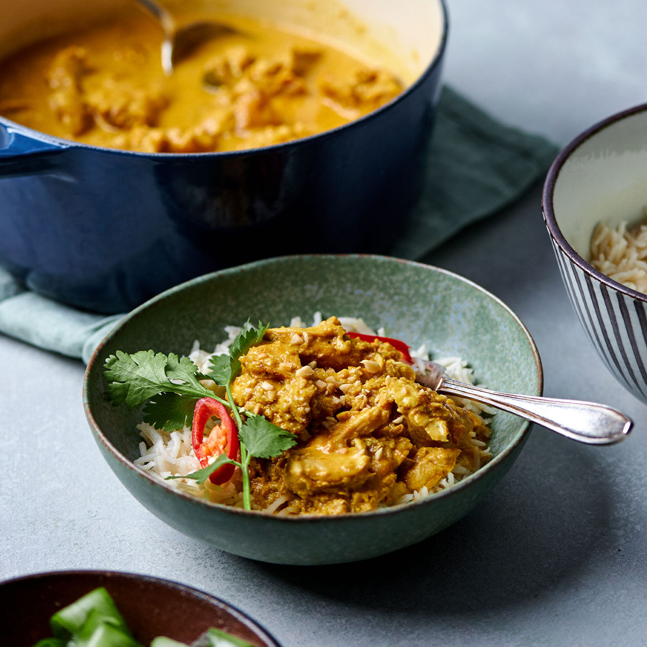 Bowl of Satay Chicken curry served over rice with coriander and chilli garnish.