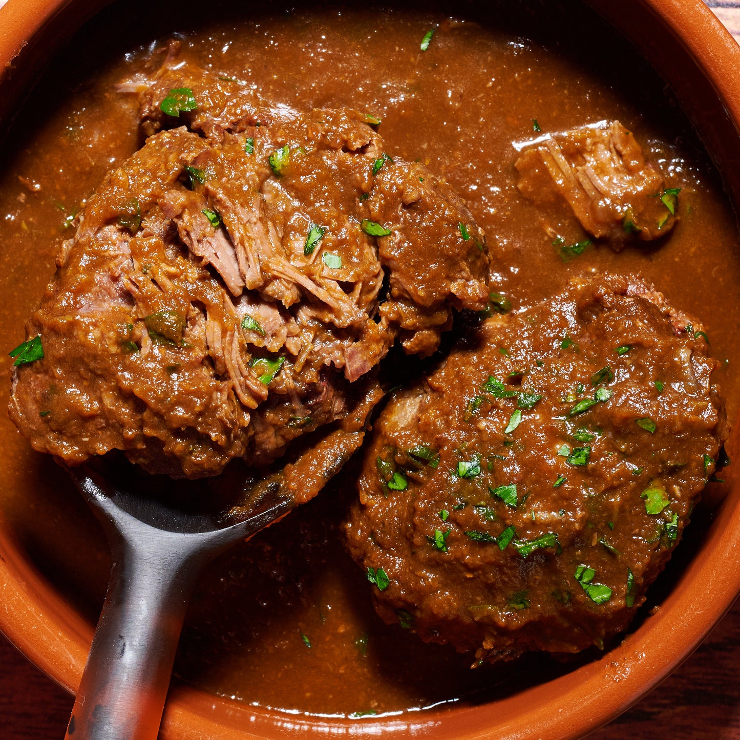Close-up of two beef cheeks in thick spiced sauce, garnished with fresh parsley.