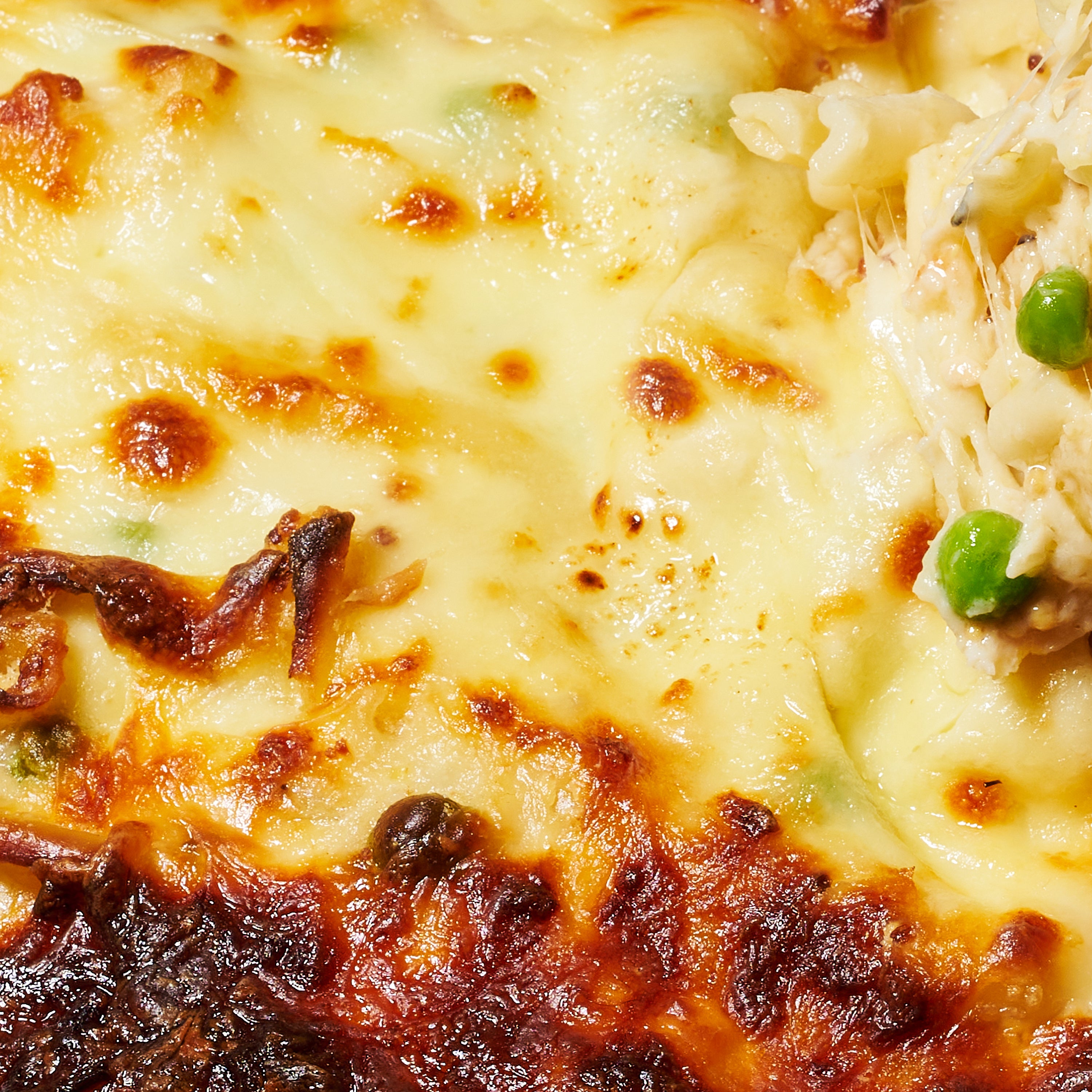 Close-up of the lasagne-style pasta al forno, showing melted cheese and hints of green peas peeking through.
