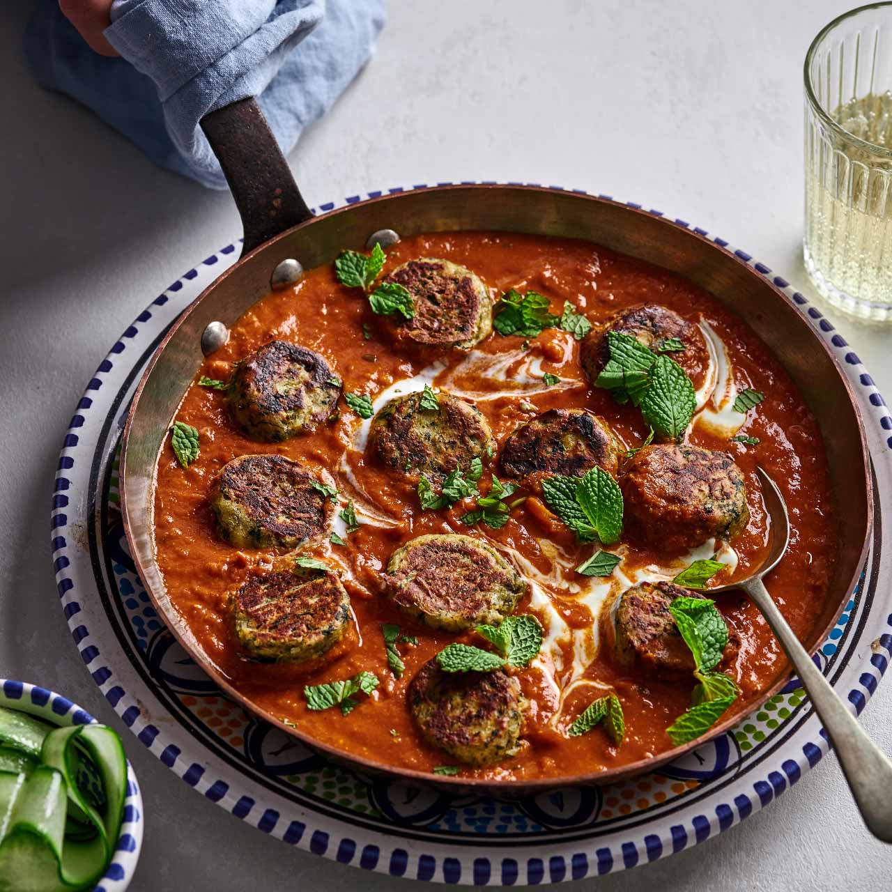 A pan of golden spinach and paneer koftas simmering in rich tomato sauce, garnished with fresh mint and swirls of yoghurt.