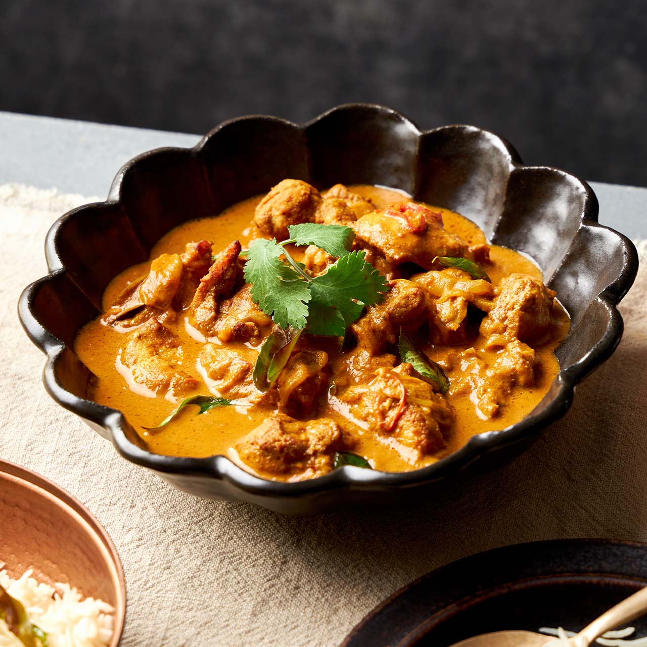 Sri Lankan Chicken Curry with tender chicken simmered in spiced coconut-tomato sauce, garnished with coriander in a black bowl.