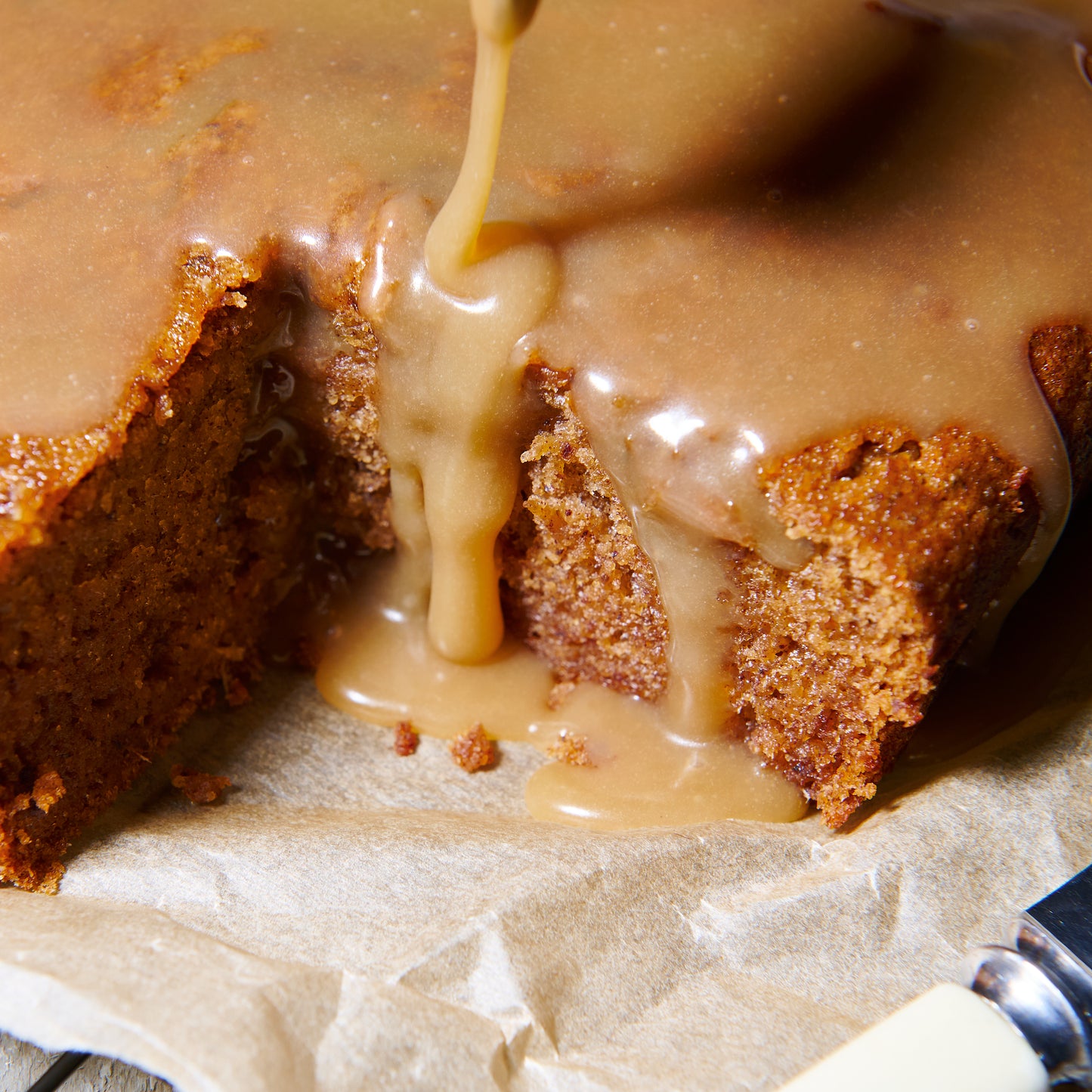 Close-up of sticky date pudding with warm caramel sauce being poured over a cut slice, highlighting its moist, fluffy texture.