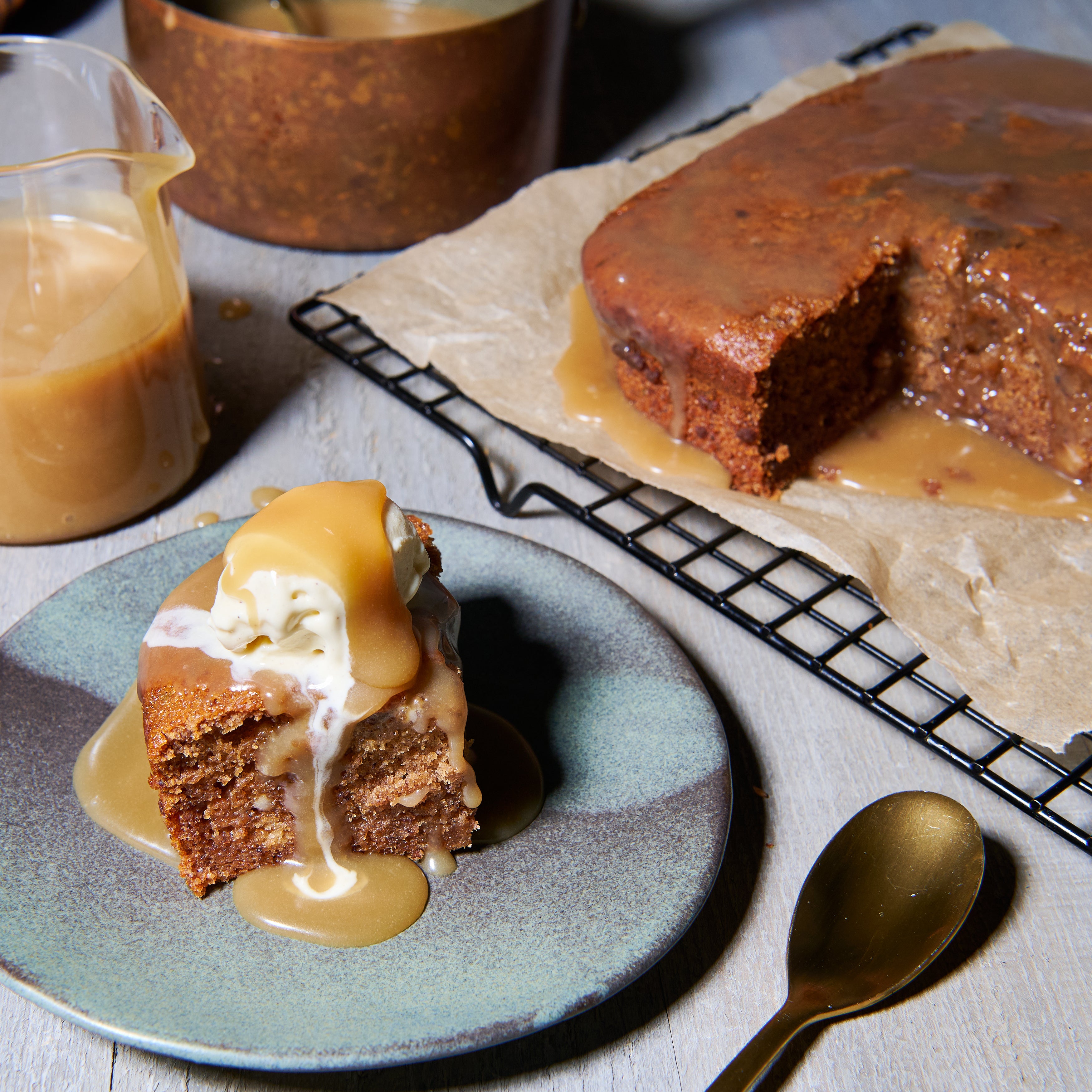 A plated serving of sticky date pudding topped with vanilla ice cream and drizzled with caramel sauce, next to the full pudding loaf.