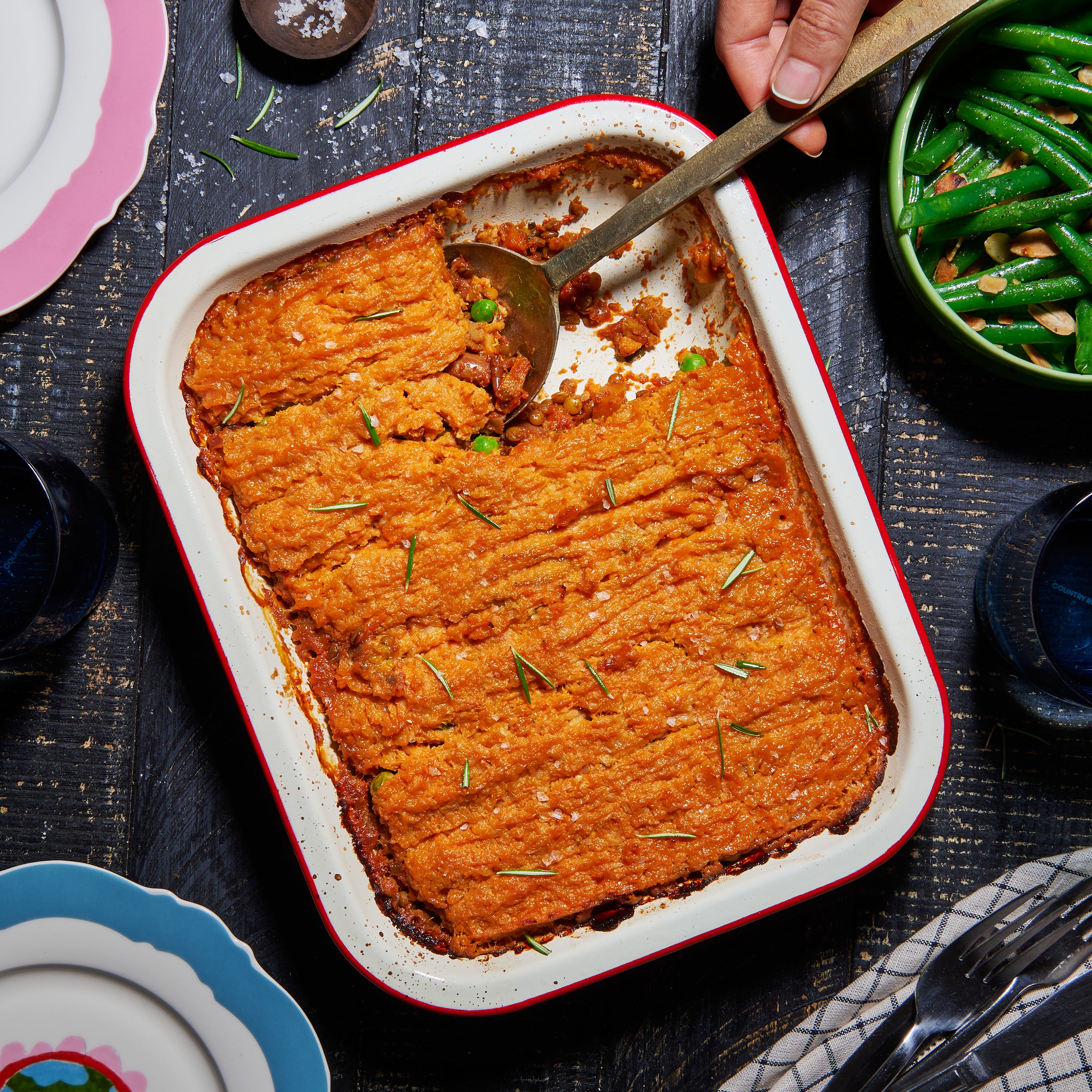 Overhead view of a golden-baked vegetable cottage pie topped with cauliflower and sweet potato mash in a white enamel baking dish.