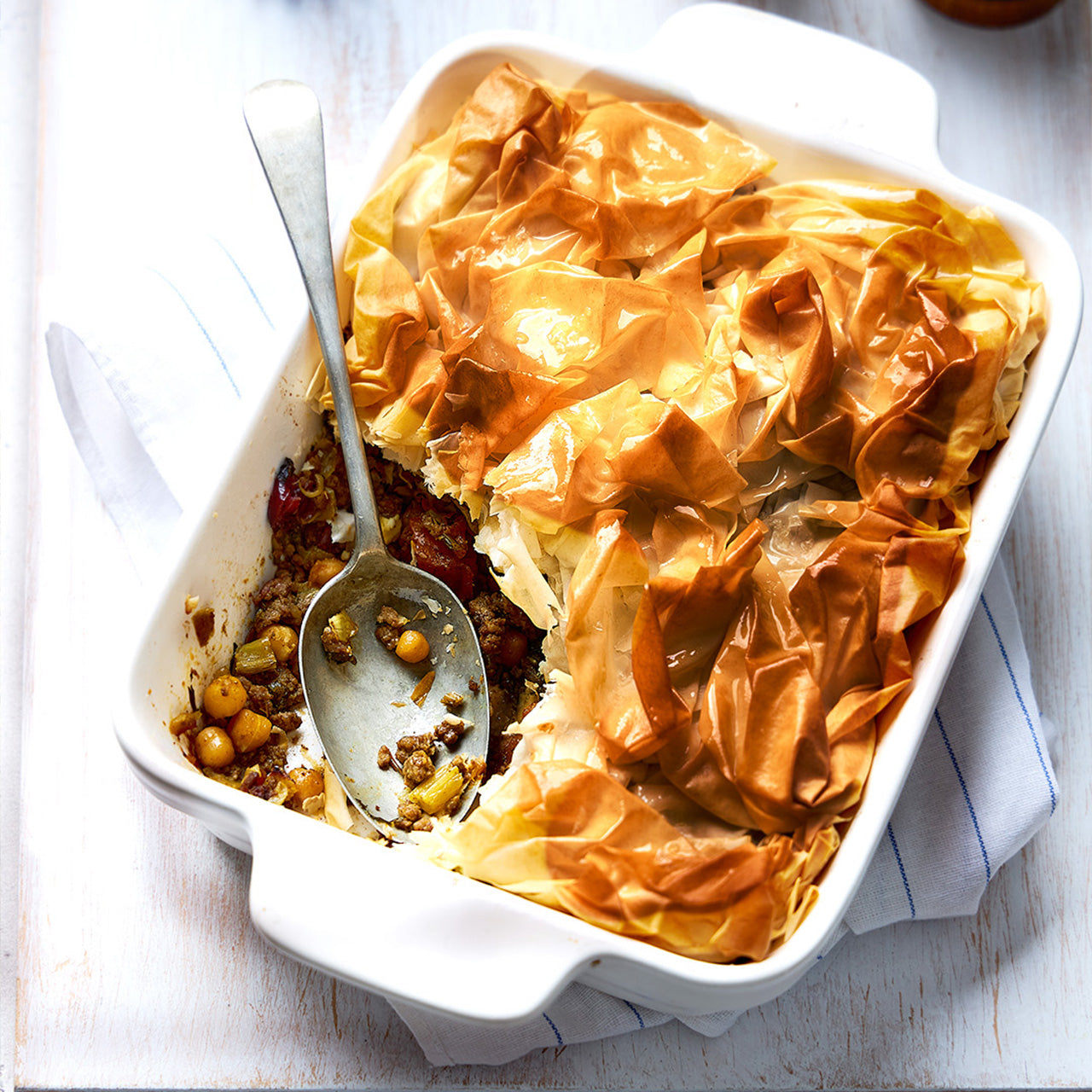 Golden filo pie with crisp pastry topping and a spoonful removed, revealing Moroccan lamb, sweet potato, chickpeas, and feta filling.