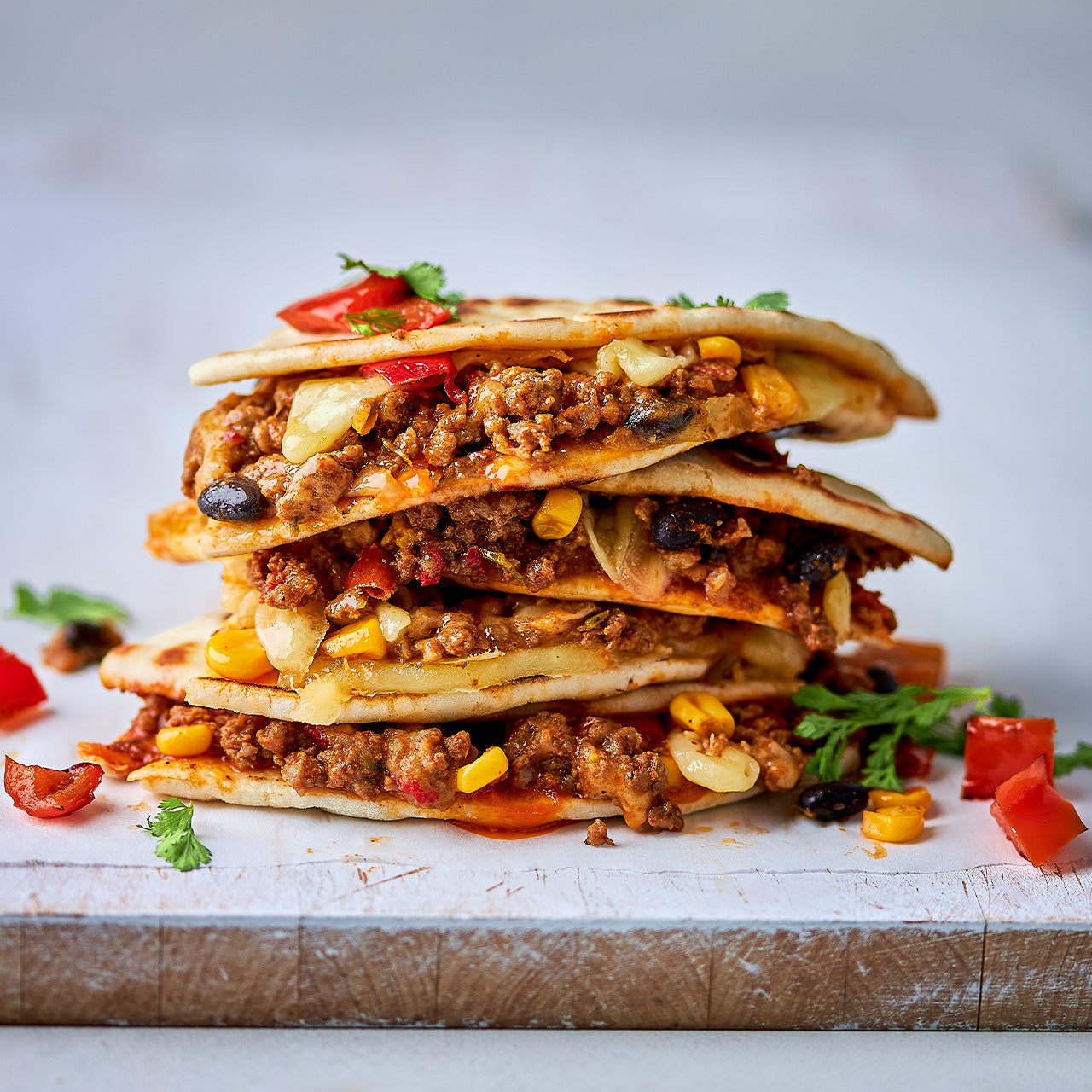 Stack of cheesy beef and black bean quesadillas with corn, capsicum and melted cheese in golden toasted tortillas.