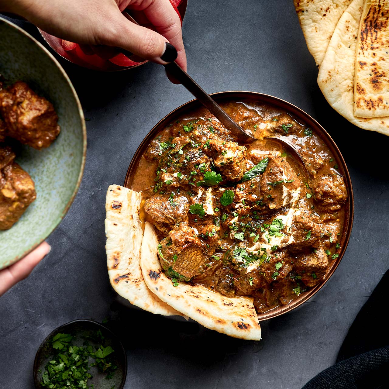 Lamb Roghan Josh served in a bowl with tender lamb in rich masala curry, garnished with coriander and paired with warm naan bread.