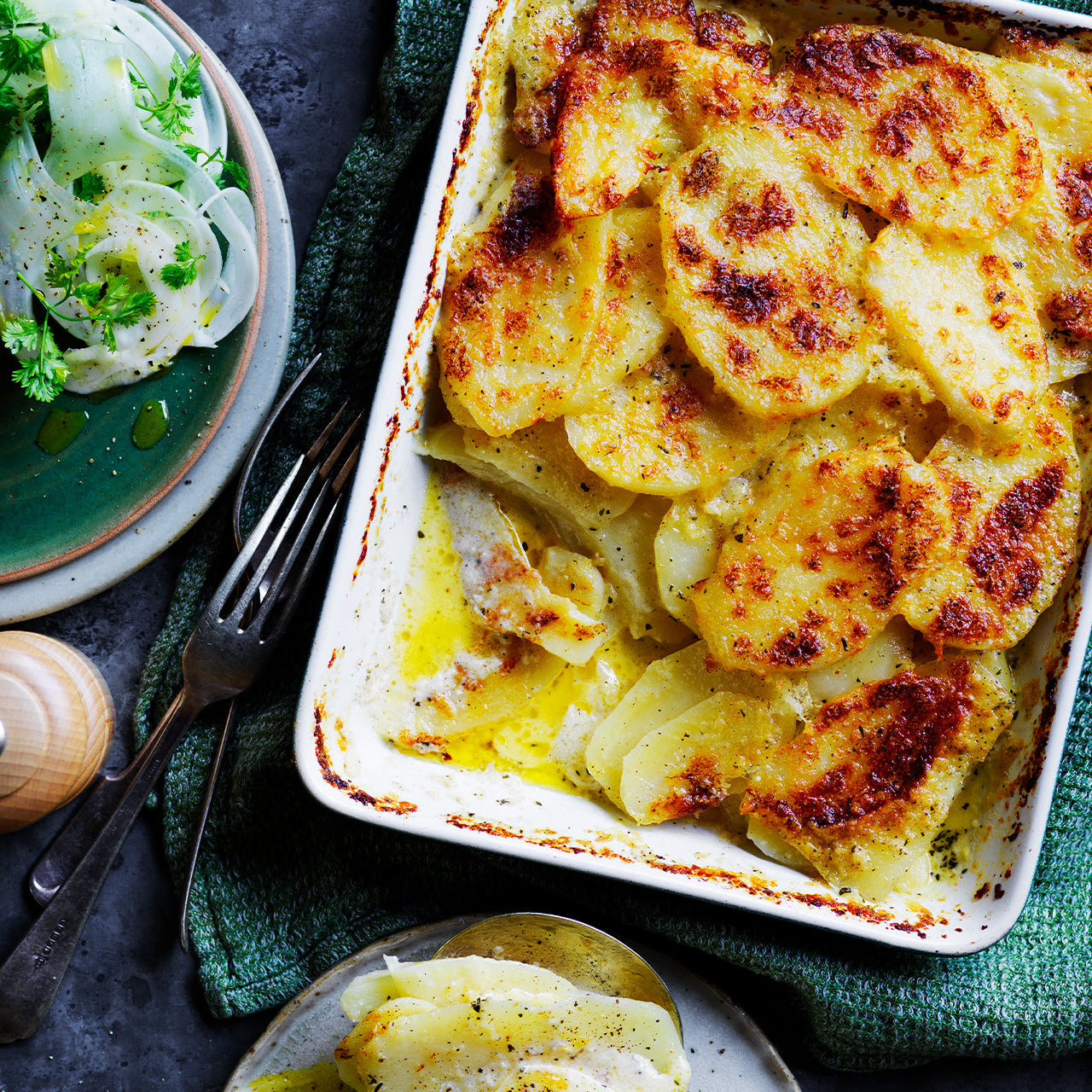 Potato Gratin baked with thinly sliced potatoes in garlic-Parmesan cream, topped with golden Gruyere cheese, served in a baking dish.