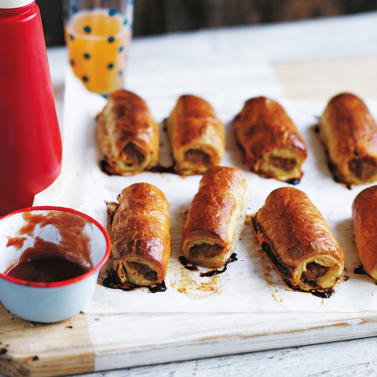 Golden puff pastry sausage rolls filled with lean pork, hidden veggies and chickpeas, baked on a tray and served with sauce.