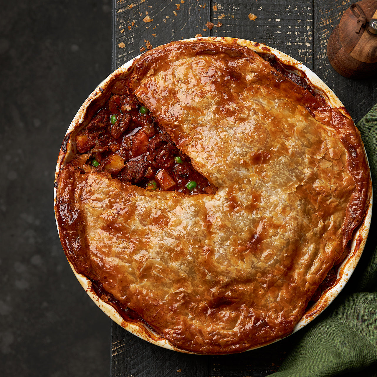 Overhead view of a family-sized beef and vegetable pie in a round baking dish with golden crust.