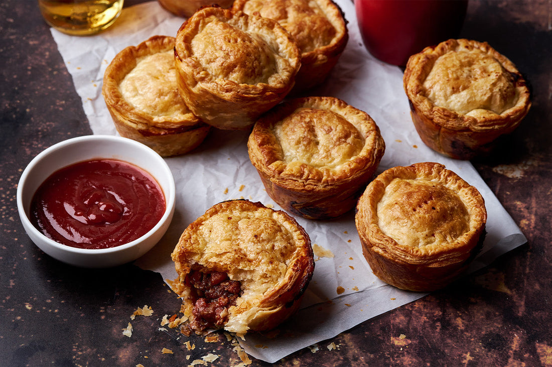 Golden mini meat pies on baking paper with a bowl of tomato sauce, showing versatile Dinner Ladies dish ideas.