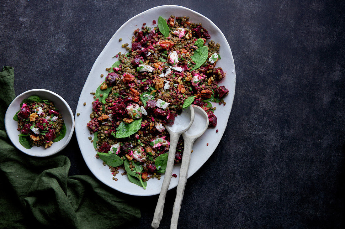 Colourful roasted vegetable and grain salad served on a white platter with spinach, beetroot, and feta.