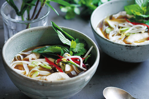 Bowls of chicken pho with noodles, herbs, chilli, and bean sprouts.