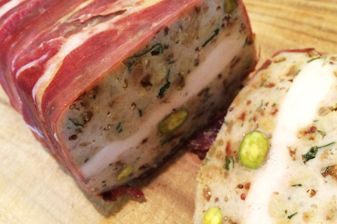 Slice of chicken and pistachio terrine wrapped in prosciutto on a wooden board.