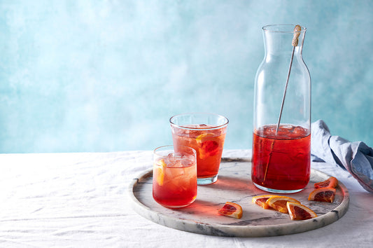 Glasses and a jug of cranberry spritz with citrus slices on a marble tray.