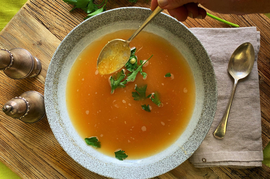 Bowl of stracciatella soup with herbs, served with a spoon on a wooden board.