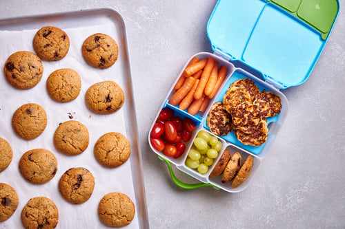 Tray of baked cookies and kids’ lunchbox with fruit, veggies, and mini cookie treats.