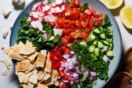 Bowl of fattoush salad with tomatoes, cucumber, radish, onion, herbs, and pita chips.