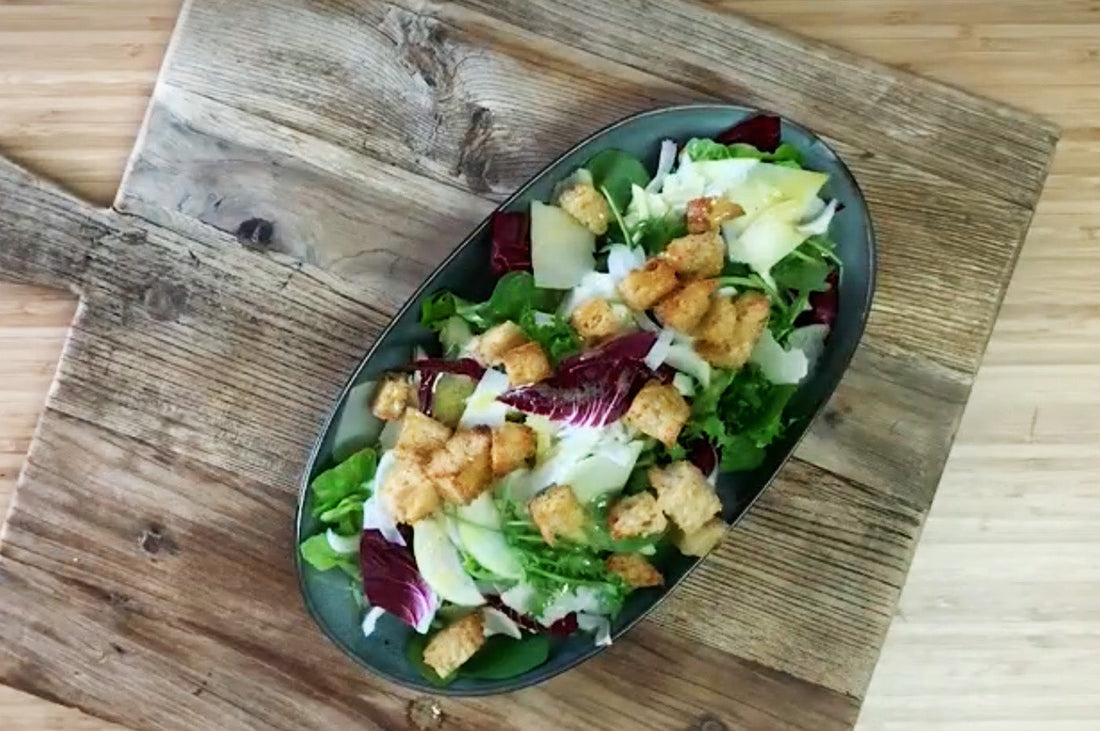 Green salad with fennel, pear, Parmesan, and croutons served on a wooden board.
