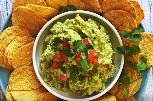 Bowl of guacamole topped with tomato and coriander, surrounded by tortilla chips.