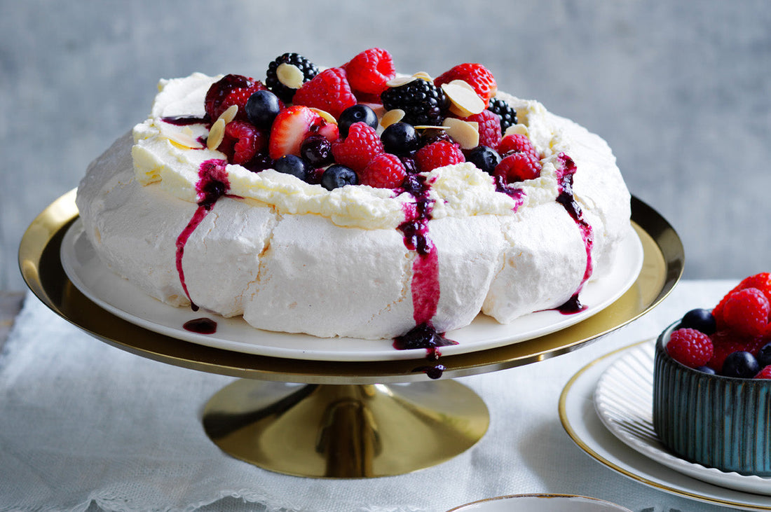 Pavlova topped with fresh berries and cream on a cake stand.