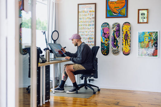 Artist Jake Foreman working at his desk with skateboards and artwork displayed on the wall.