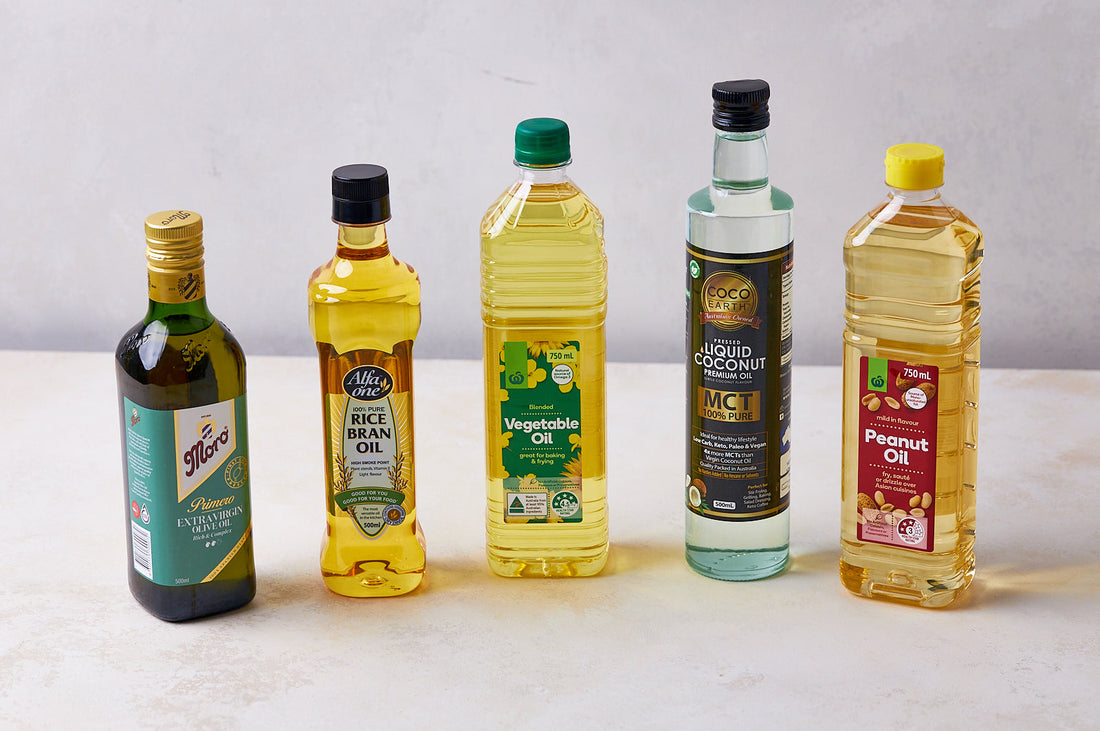Five bottles of different cooking oils, including olive and vegetable oil, displayed on a neutral surface.
