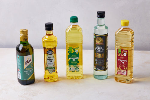Five bottles of different cooking oils, including olive and vegetable oil, displayed on a neutral surface.